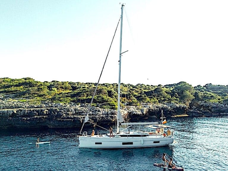Segelboot mit Personen und Paddleboards vor felsiger Küste.